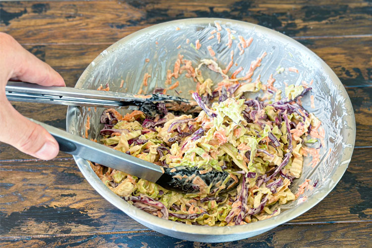 tongs mixing cabbage and dressing together