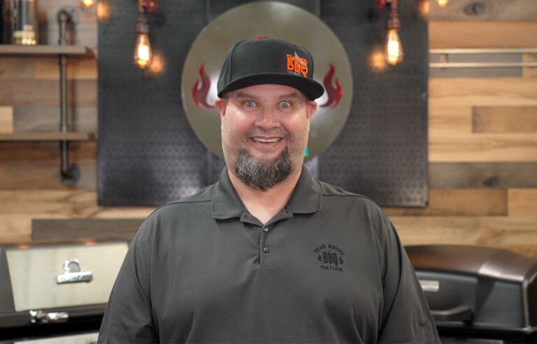 man standing in front of two gas grills smiling