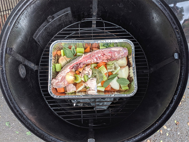 a drip pan with meat and vegetables inside the smoker