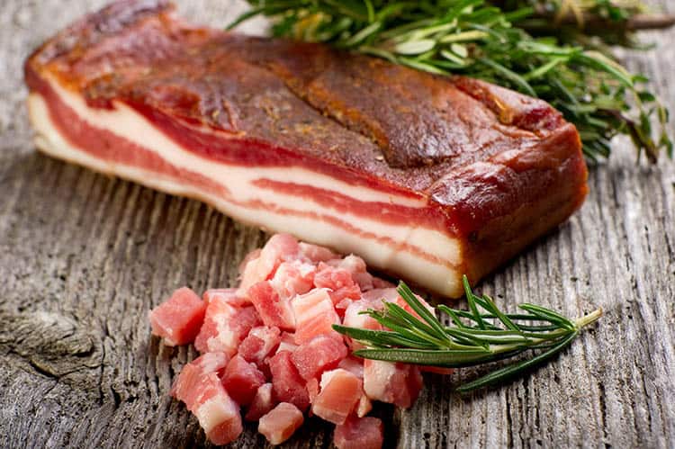 a slab of bacon with rosemary on a wooden table