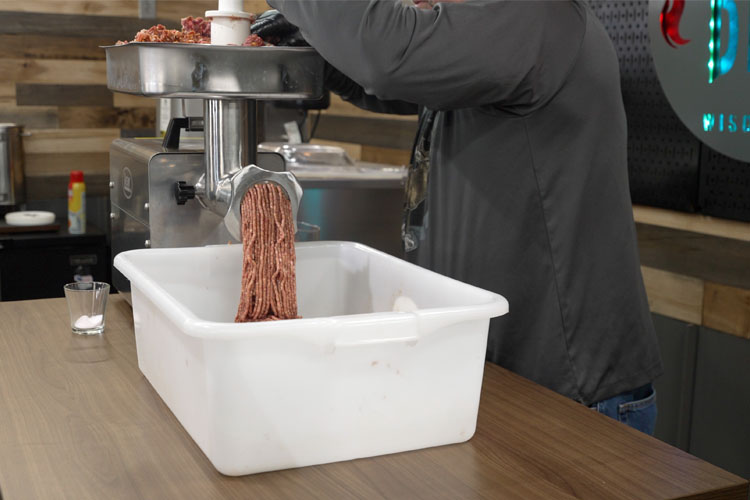 meat being extruded from a grinder in a white tub