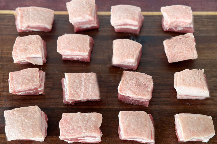 cubed pork belly on wooden chopping board