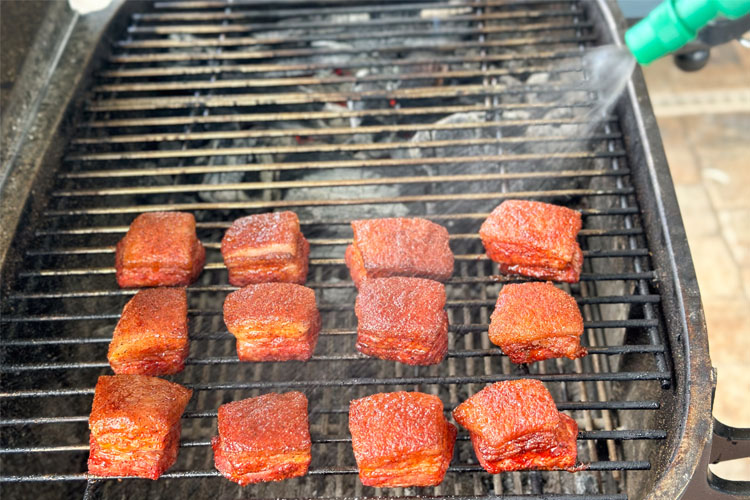 cooked pork belly cubes in the smoker being sprayed