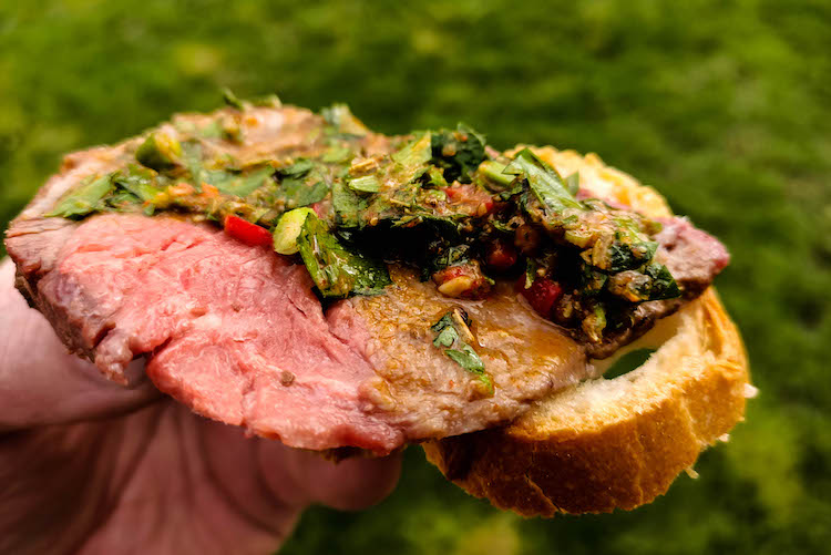A piece of bread with meat and chimichurri sauce