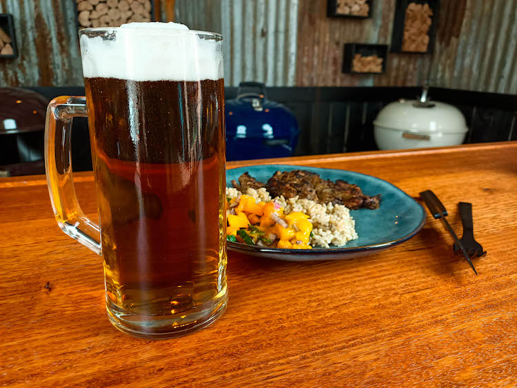 a glass of beer with jerk chicken thighs, rice and mango salsa