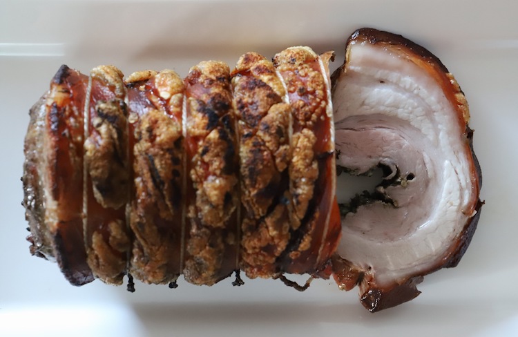 cooked and sliced porchetta style pork belly on a white plate