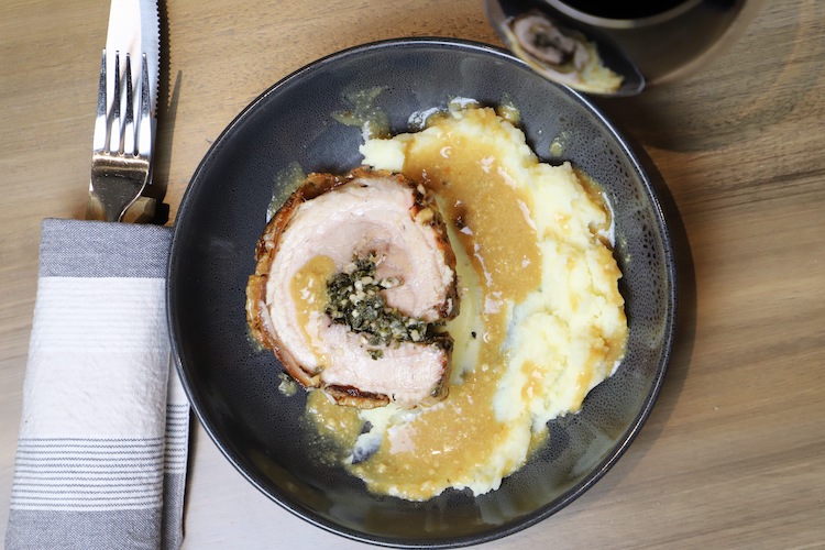 a slice of porchetta style pork belly on a plate with mashed potatoes and gravy