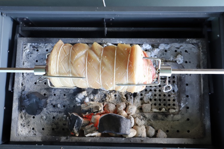 uncooked pork belly on a rotisserie over charcoal