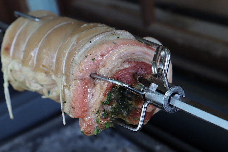 pork belly on a rotisserie with a wireless meat thermometer probe
