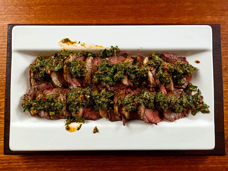 slices of Brazilian picanha steak drizzled with chimichurri on a plate