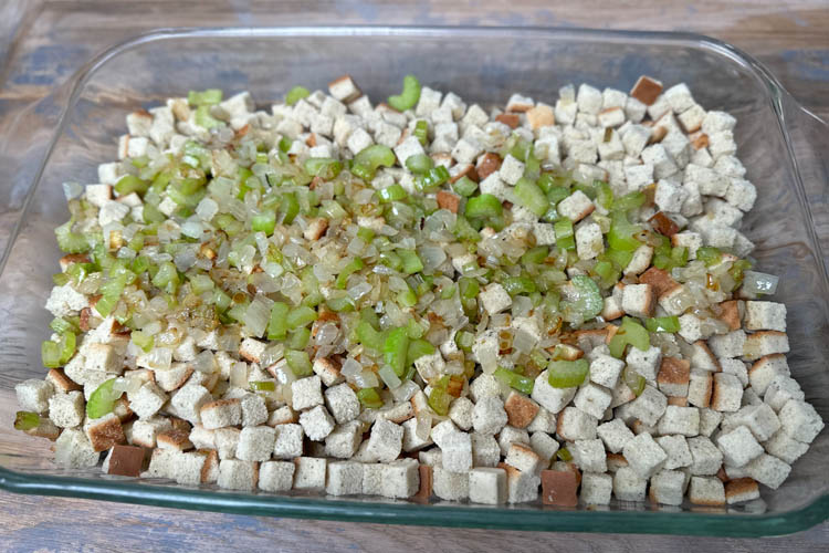 onion and celery on top of bread cubes in glass tray