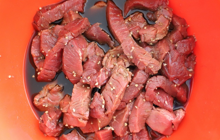 sliced beef in marinade in a plastic bowl