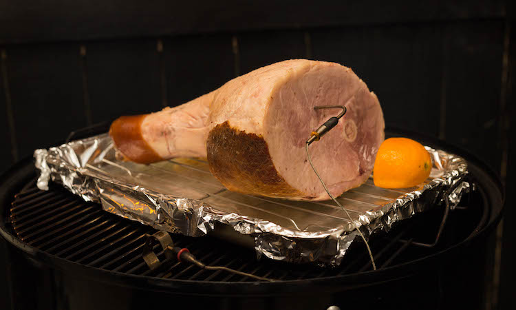 ham on a wire rack with an orange half in a smoker