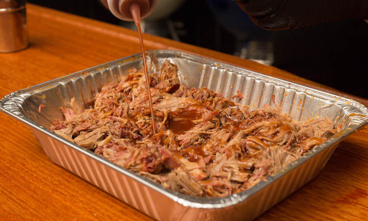poring bbq sauce in a tray with pulled pork