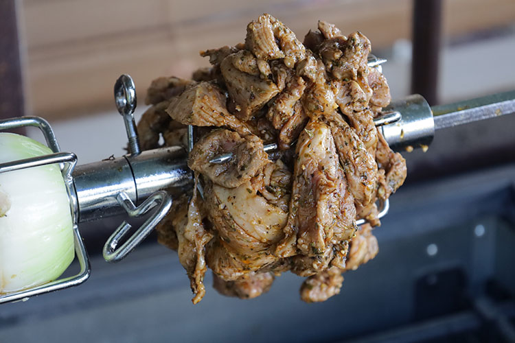 raw pieces of lamb shoulder on a rotisserie rod