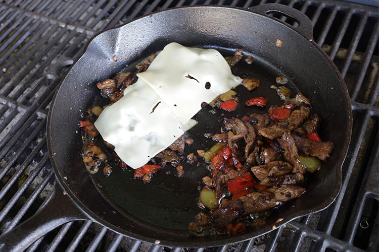 cheese slices over philly cheesesteak filling on a cast iron skillet