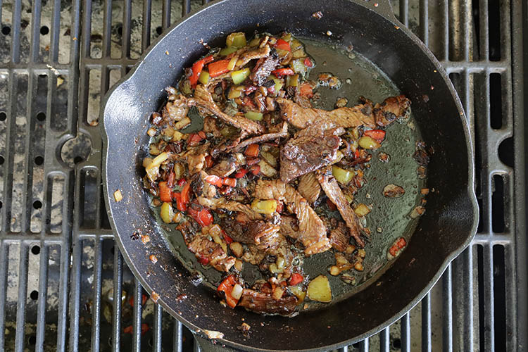 steak slices, bell peppers and onions cooking on a cast iron skillet