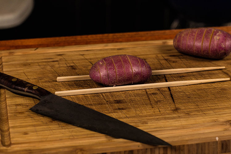 uncooked potatoes with chopsticks on a wooden cutting board