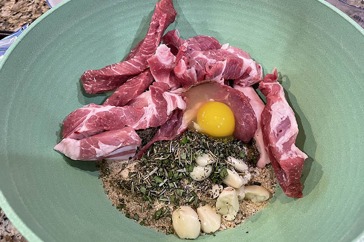 pork butt slices, raw egg, herbs and spices in a bowl