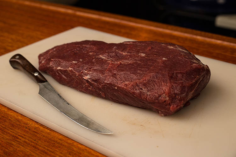 beef flat iron steak with a fat cap trimmed off on a plastic board