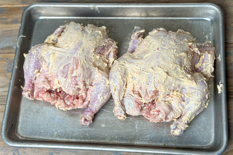 two cornish hens slathered in butter on a metal tray