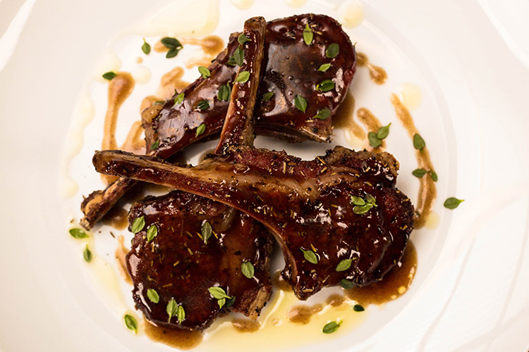 lamb cutlets with pomegranate sauce on a white plate