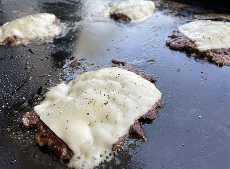 smash burger patties with cheese cooking on a griddle