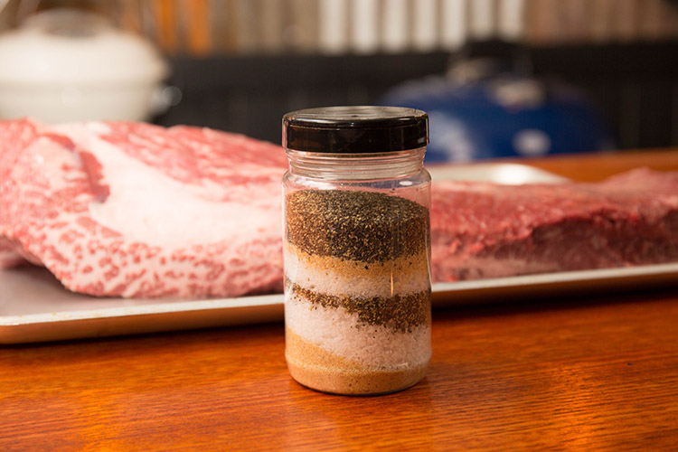 salt pepper garlic seasoning in a clear rub shaker with beef brisket on the background