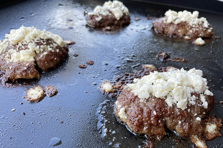 lamb burger patties with feta cheese cooking on a griddle