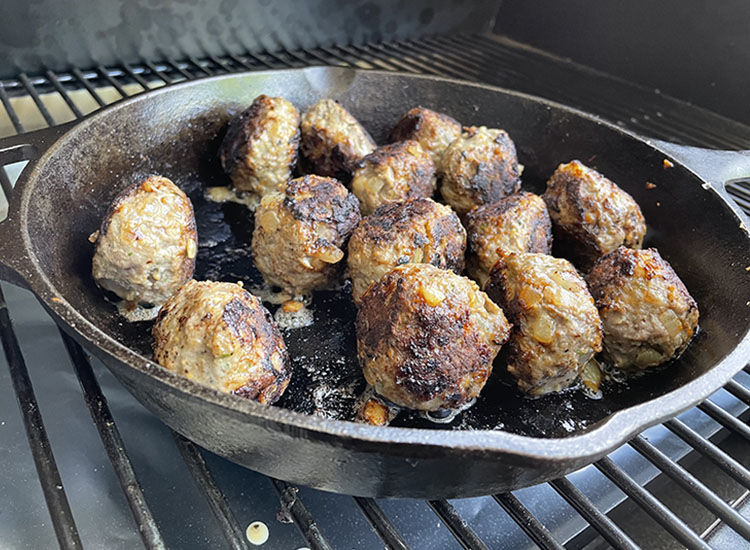 seared venison meatballs on a cast iron pan on a pellet grill