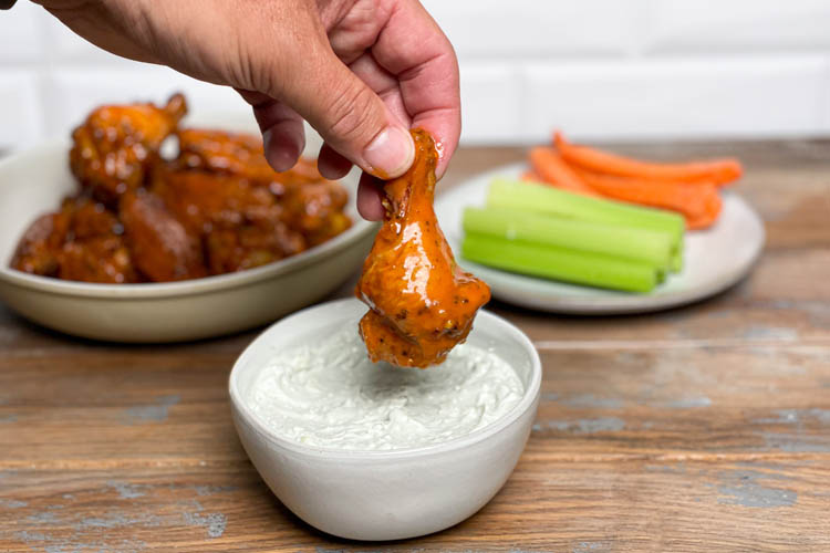 bowl of ranch dressing with a wing being dipped into it