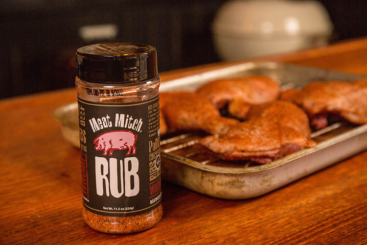 a jar of Meat Mitch Rub with seasoned chicken legs in the background