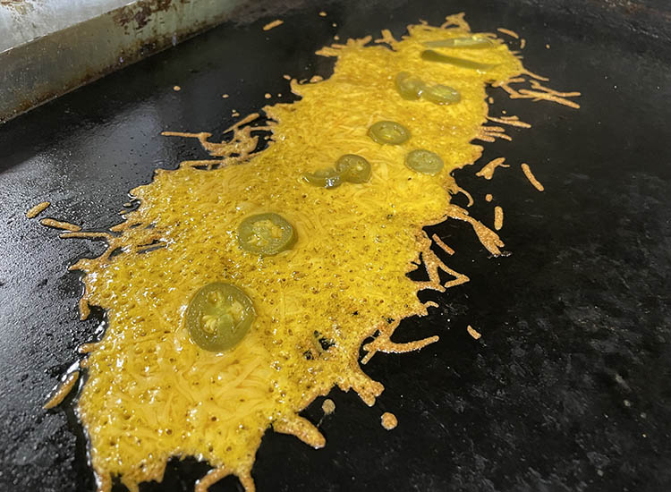 melted cheese and pieces of jalapeno peppers on a griddle