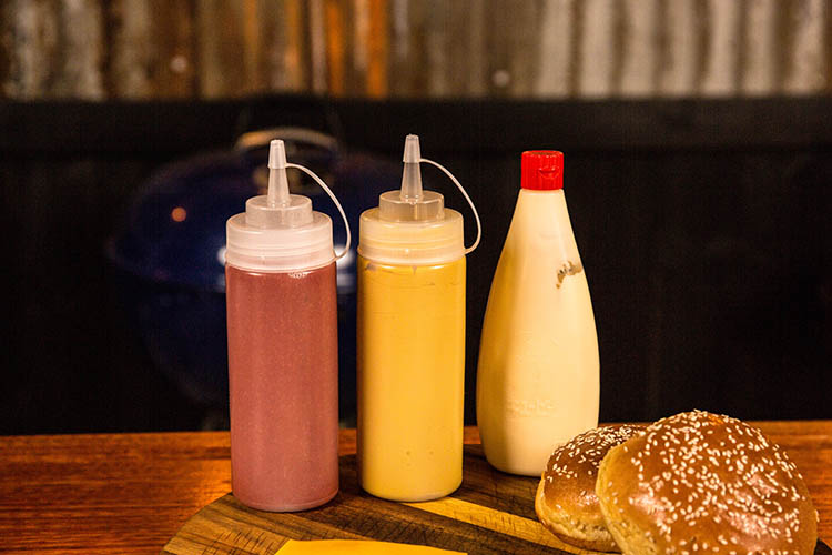 bottles with mustard, ketchup and mayonnaise on a wooden board