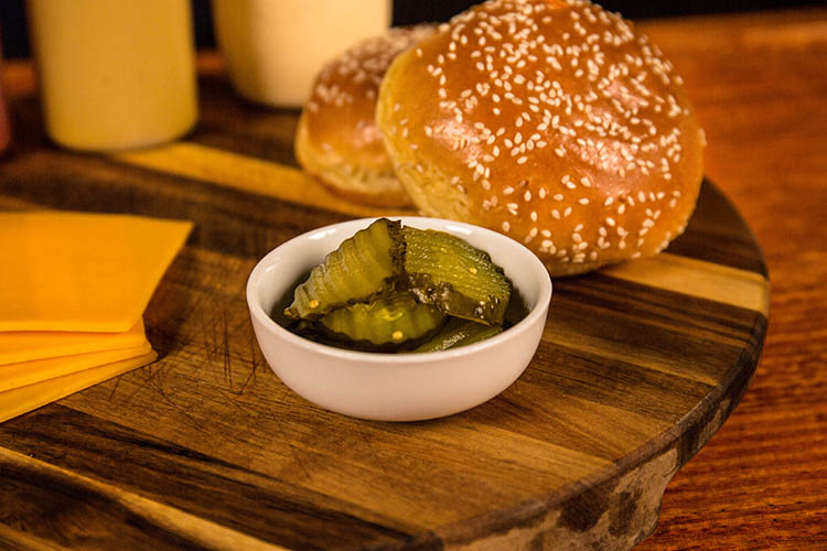 sliced pickles, cheese and burger buns on a wooden table