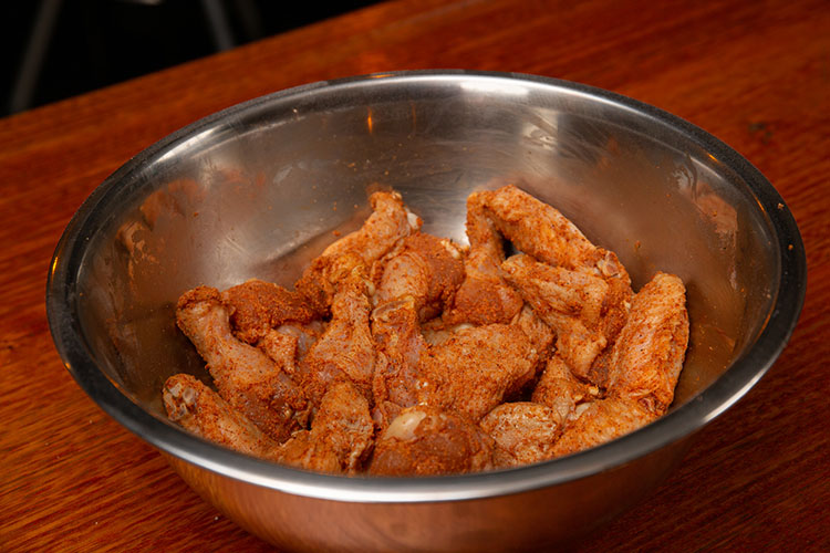 Seasoned raw chicken wings in a metal bowl