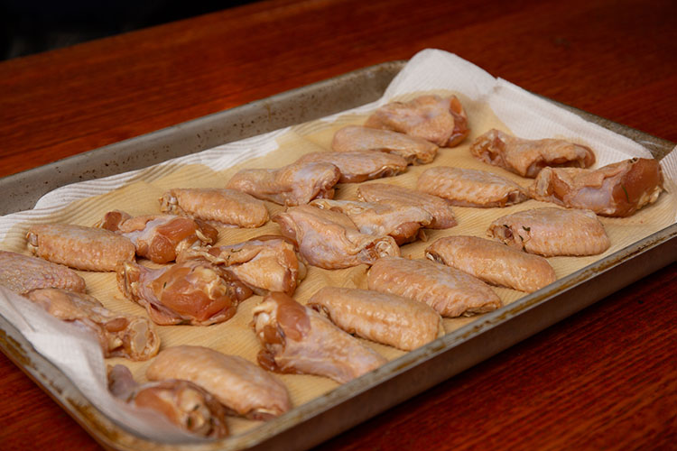 Raw chicken wings being dried on paper towels after brining