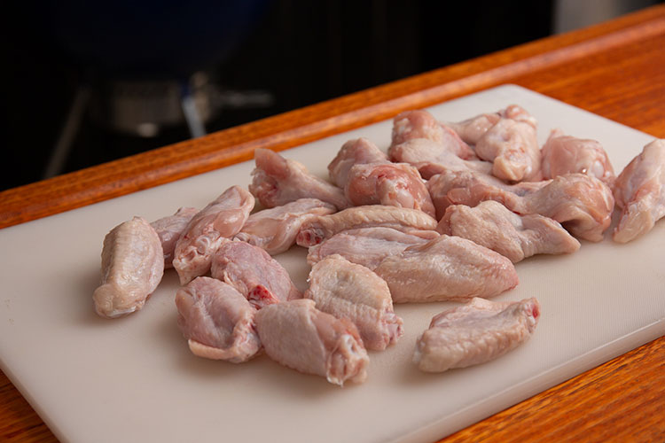 Prepped raw chicken wings on a white chopping board