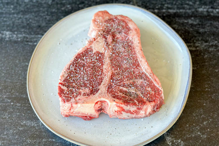 seasoned raw porterhouse steak on a white plate