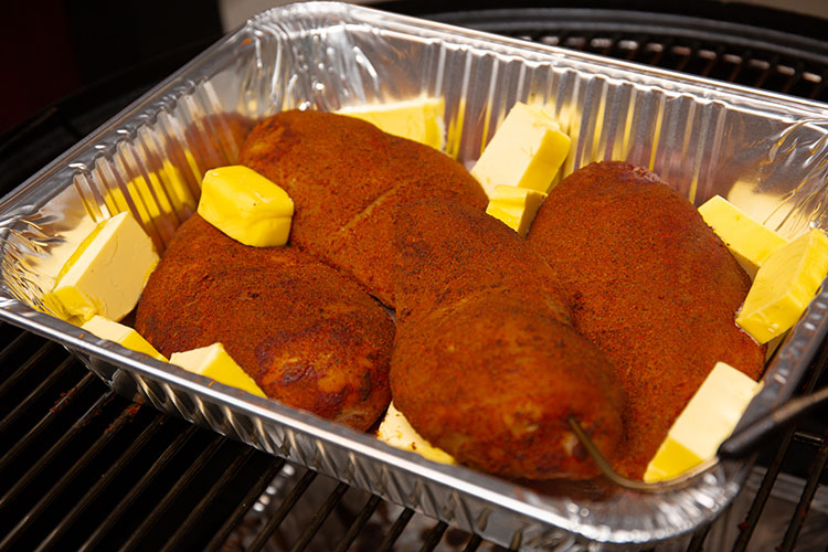 Smoked chicken breasts in a tin tray with cubes of butter