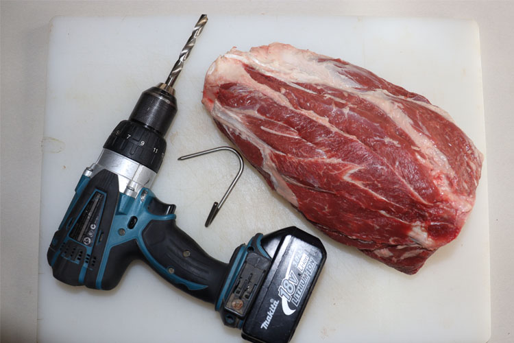 drill, hook and raw beef shank on a white chopping board