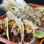 smoked beef shank tacos on a tray with grilled corn cobs, jalapeno bread and a lime cheek