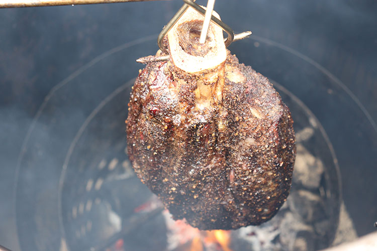 cooked beef shank hanging over charcoal