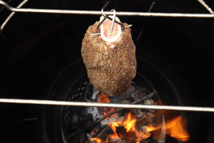 Uncooked beef shank hanging in the BBQ over lit charcoal