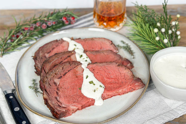 prime rib plated on white plate with horseradish sauce drizzled over it