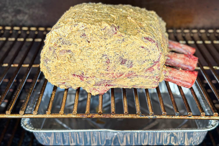 raw prime rib in the smoker with foil tray underneath