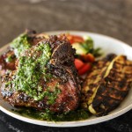 cooked lamb chops with chimichurri on a white plate with grilled veges