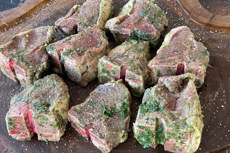 uncooked lamb chops sprinkled with salt, pepper and granulated garlic on wooden board