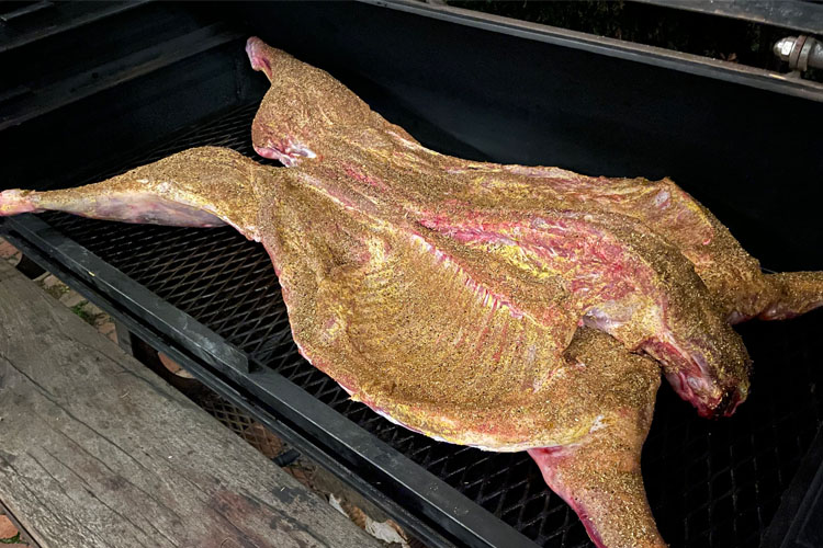 whole uncooked lamb with rub lying on smoker