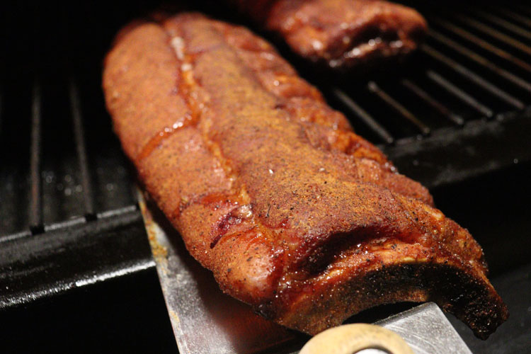 mahogany colored pork rib sitting on shelf in pellet grill